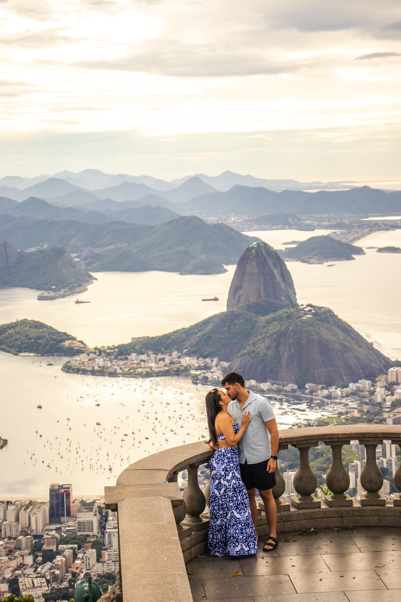 Casal se beijando no mirante do Corcovado com o Pão de Açúcar e a Baía de Guanabara ao fundo ao entardecer