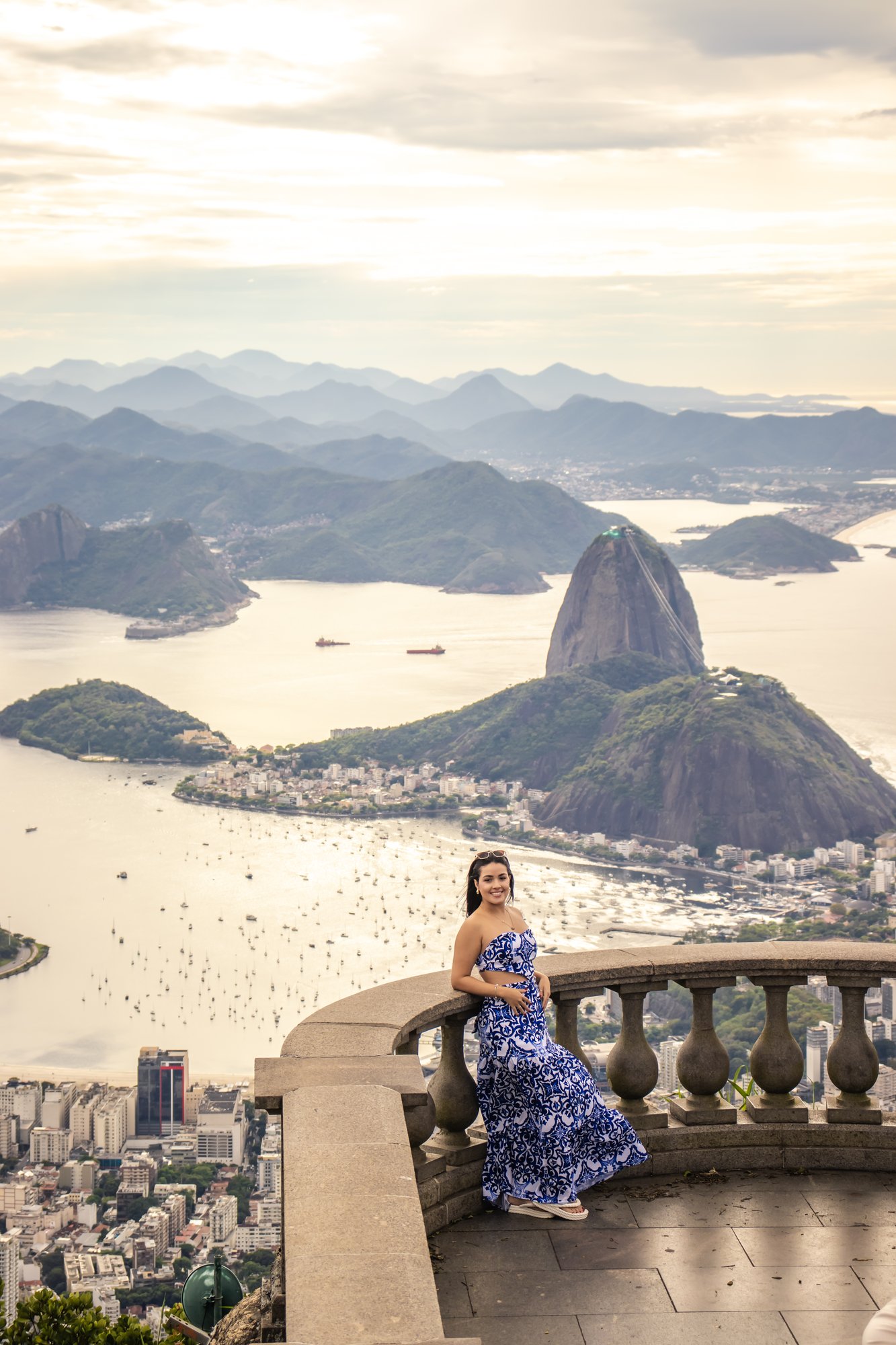 Visitante apoiada no gradil do mirante do Cristo Redentor com panorama da Baía de Guanabara e Pão de Açúcar