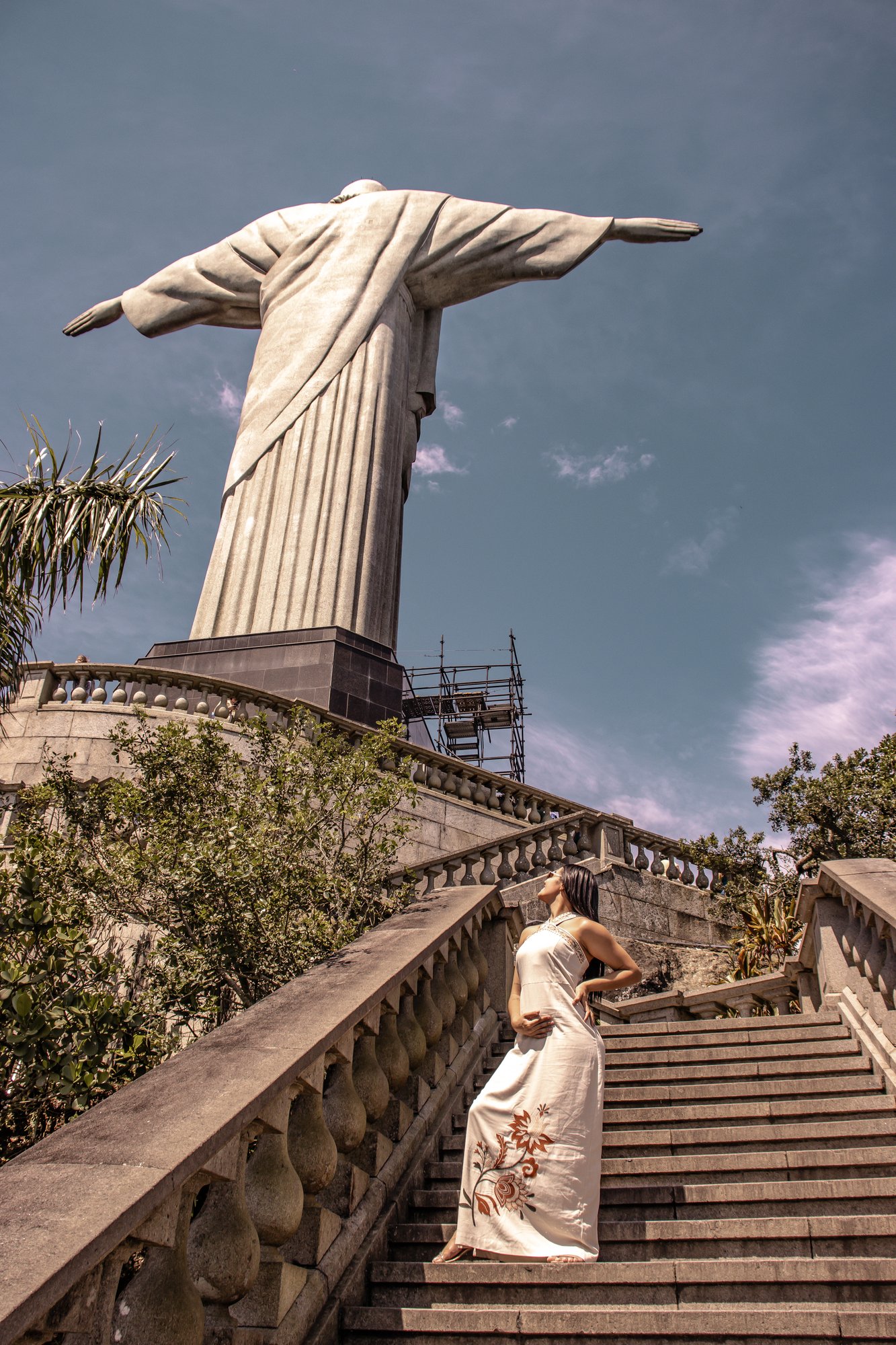 Visitante com vestido branco nas escadarias do Cristo Redentor olhando para a estátua em dia ensolarado