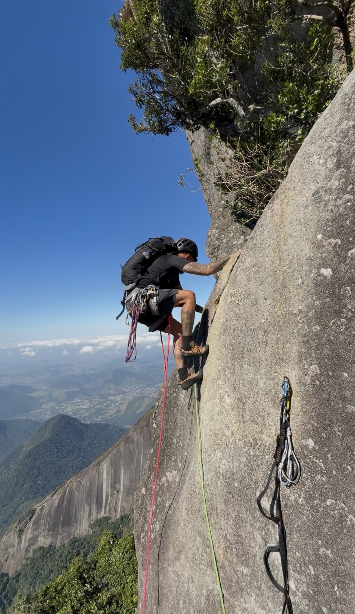 Escalador em rappel no Dedo de Deus com a parede granítica vertical e floresta da Serra dos Órgãos abaixo