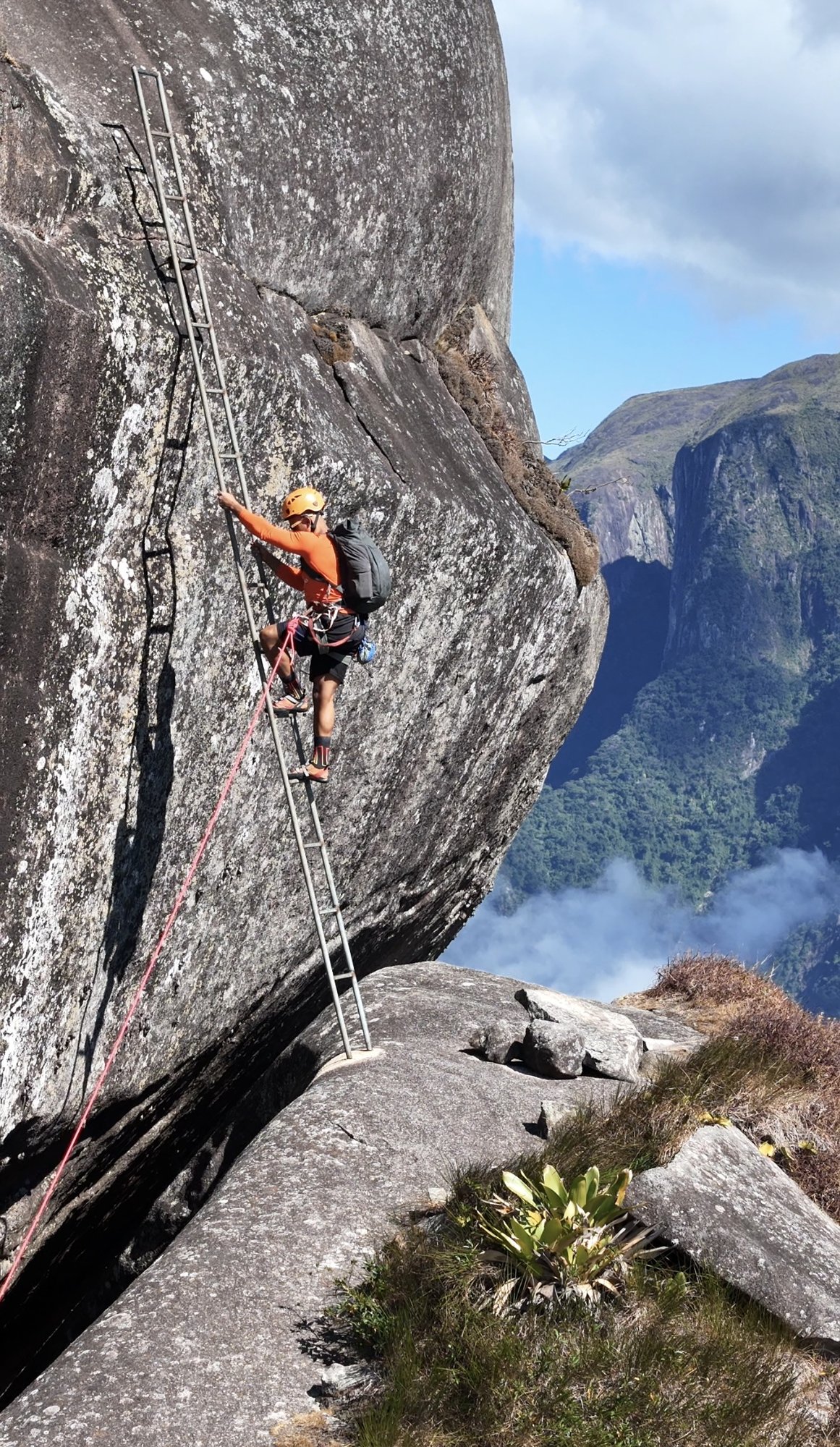 Pitch de placa no Dedo de Deus com escalador concentrado e a agulha íntegra ao fundo contra o céu