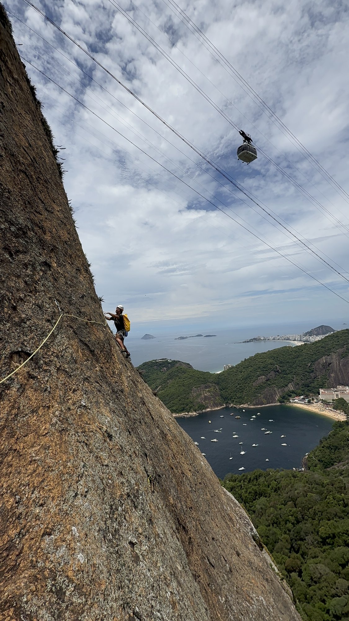 Escalador na face do Pão de Açúcar com bondinho e Praia Vermelha ao fundo