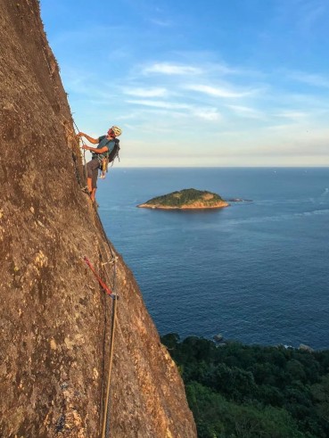 Escalador na Via Italianos ao entardecer com ilha e oceano ao fundo