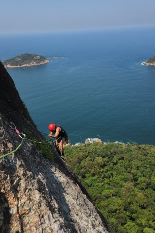 Escalador com capacete vermelho na Via Italianos do Pão de Açúcar com oceano Atlântico abaixo