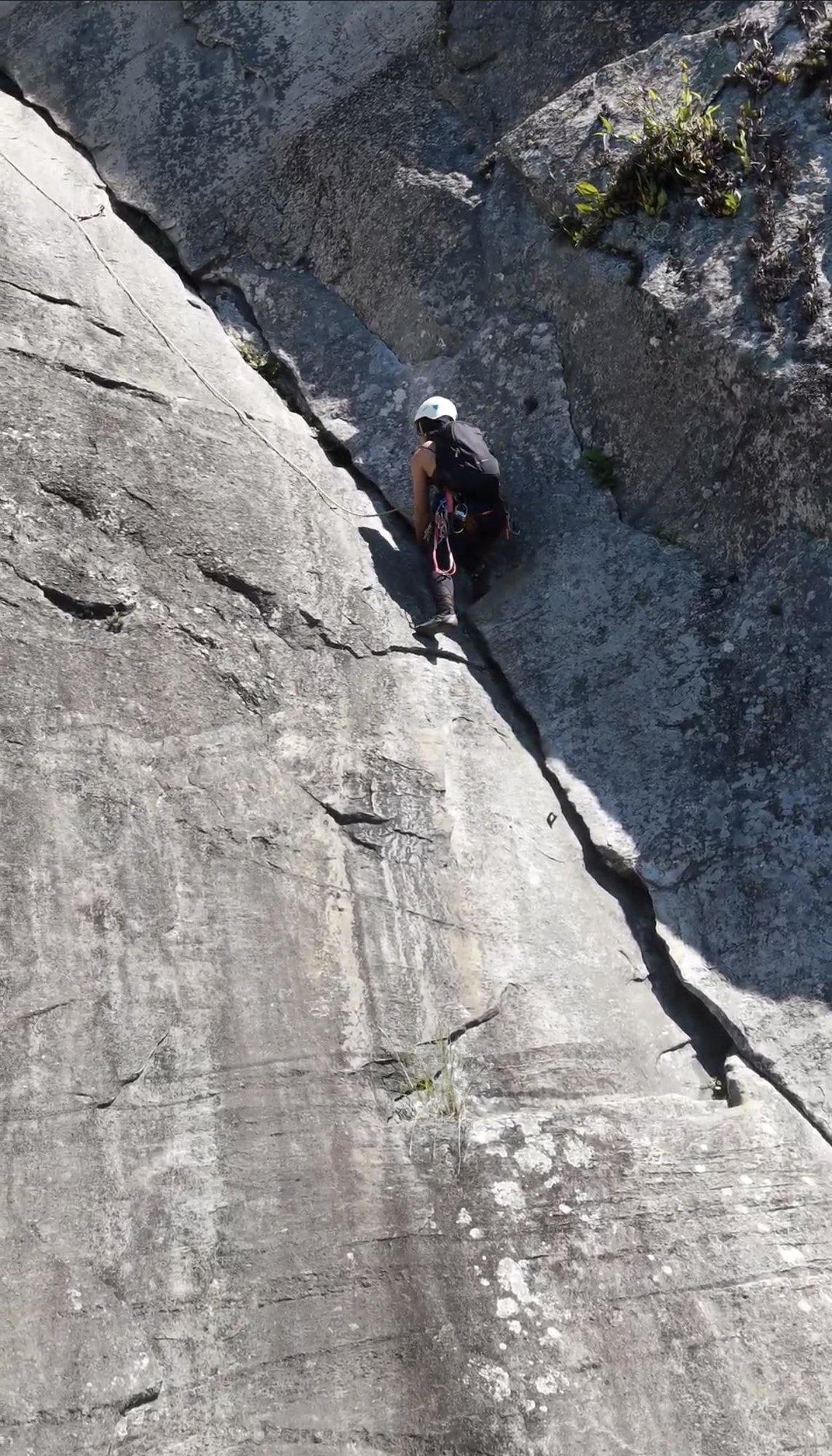 Escalador em crack vertical na face do Corcovado, capacete branco, Vista aérea