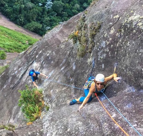 Dois escaladores na face rochosa inclinada do Corcovado com vegetação atlântica ao fundo