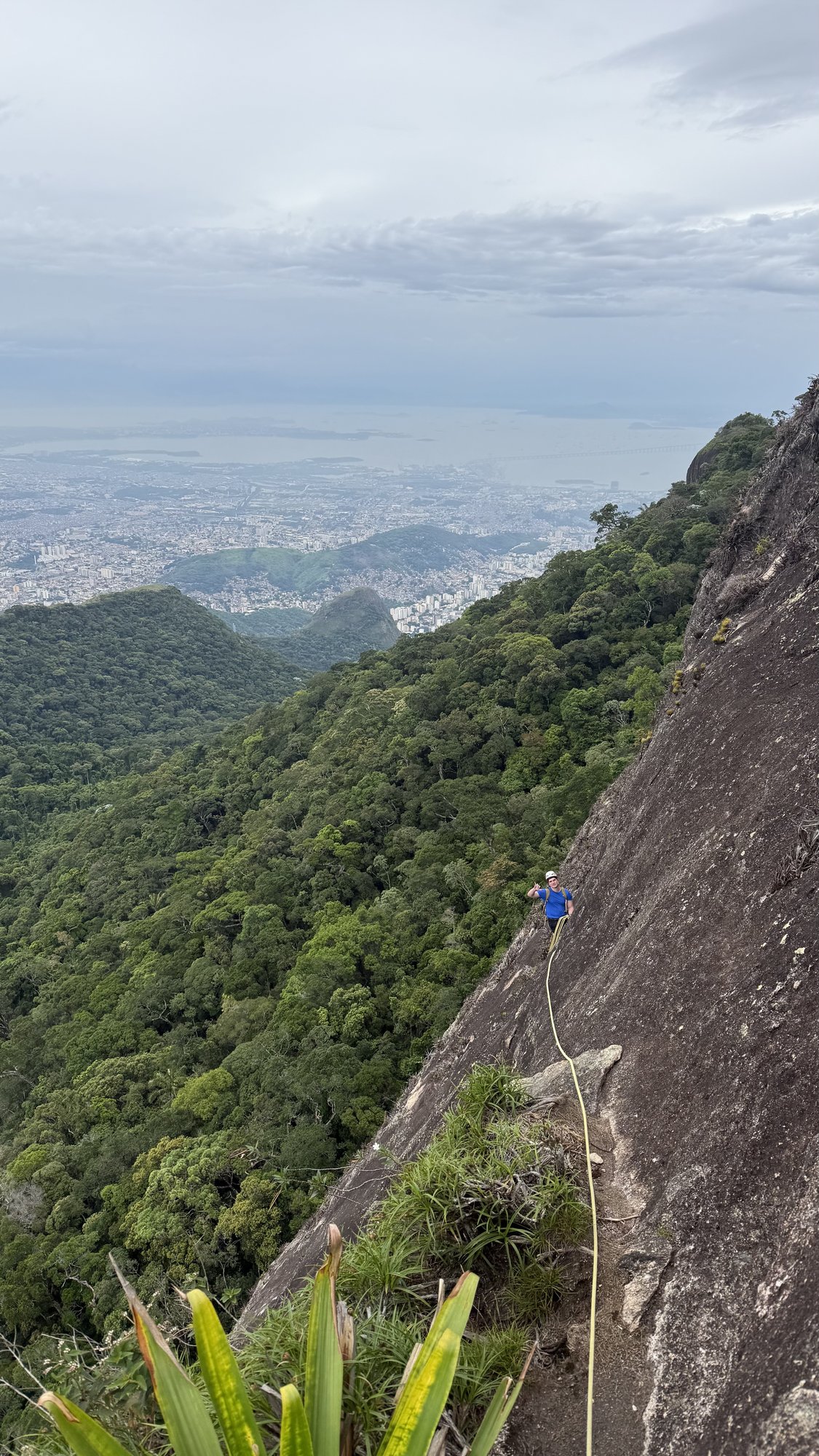 Escalador em corda na face do Pico da Tijuca com a Floresta da Tijuca e o Rio de Janeiro ao fundo