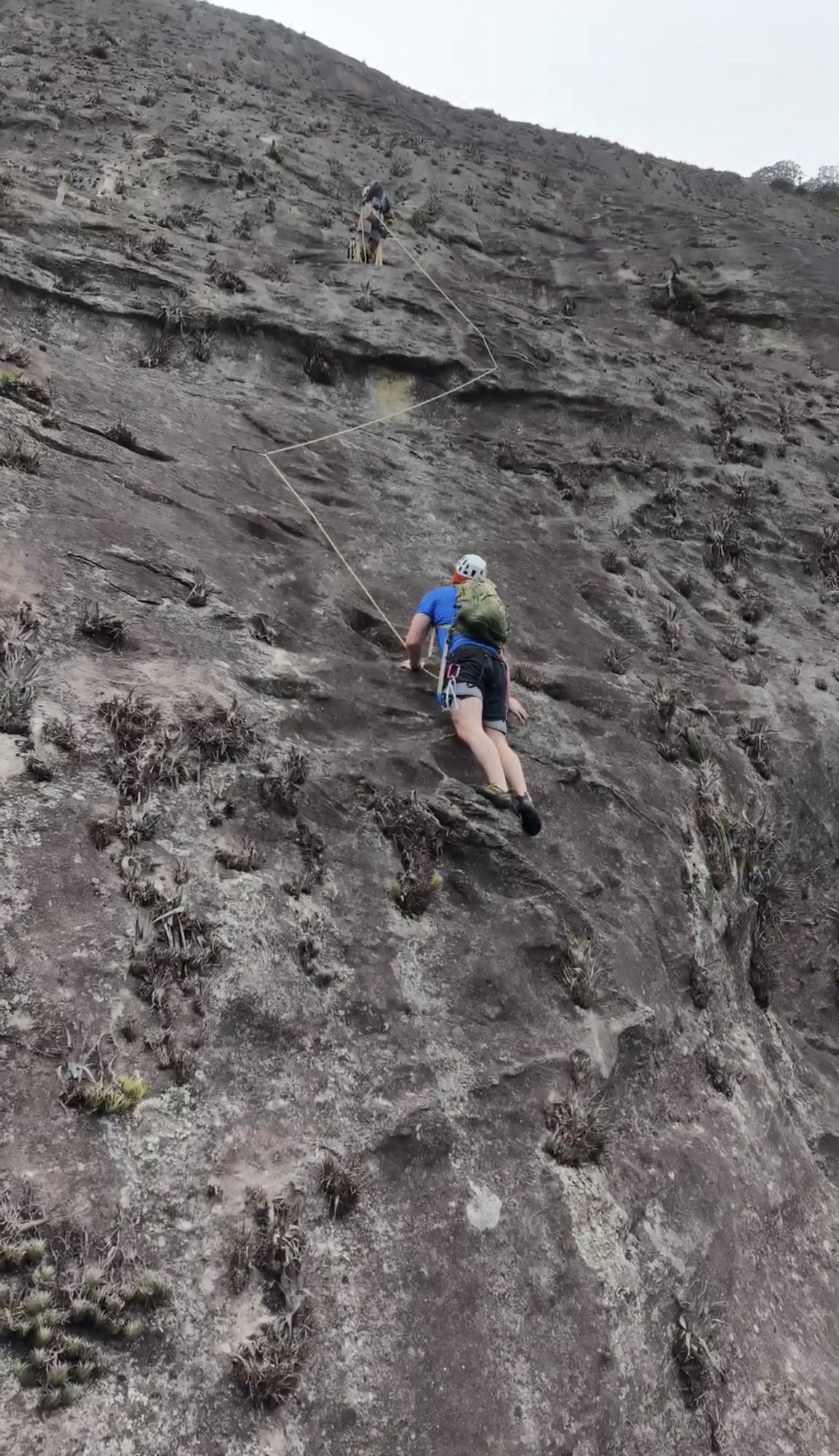 Escaladora em placa de granito escuro na face do Pico da Tijuca com vegetação ao fundo