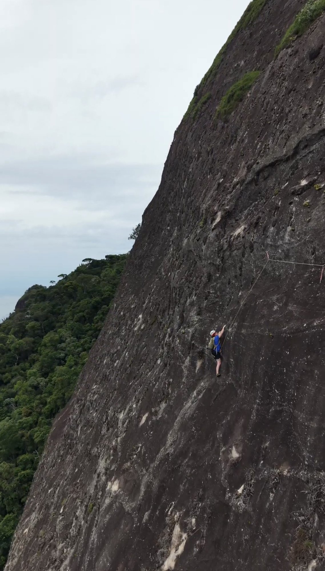 Vista ampla da face do Pico da Tijuca com escalador na parede e Floresta da Tijuca abaixo