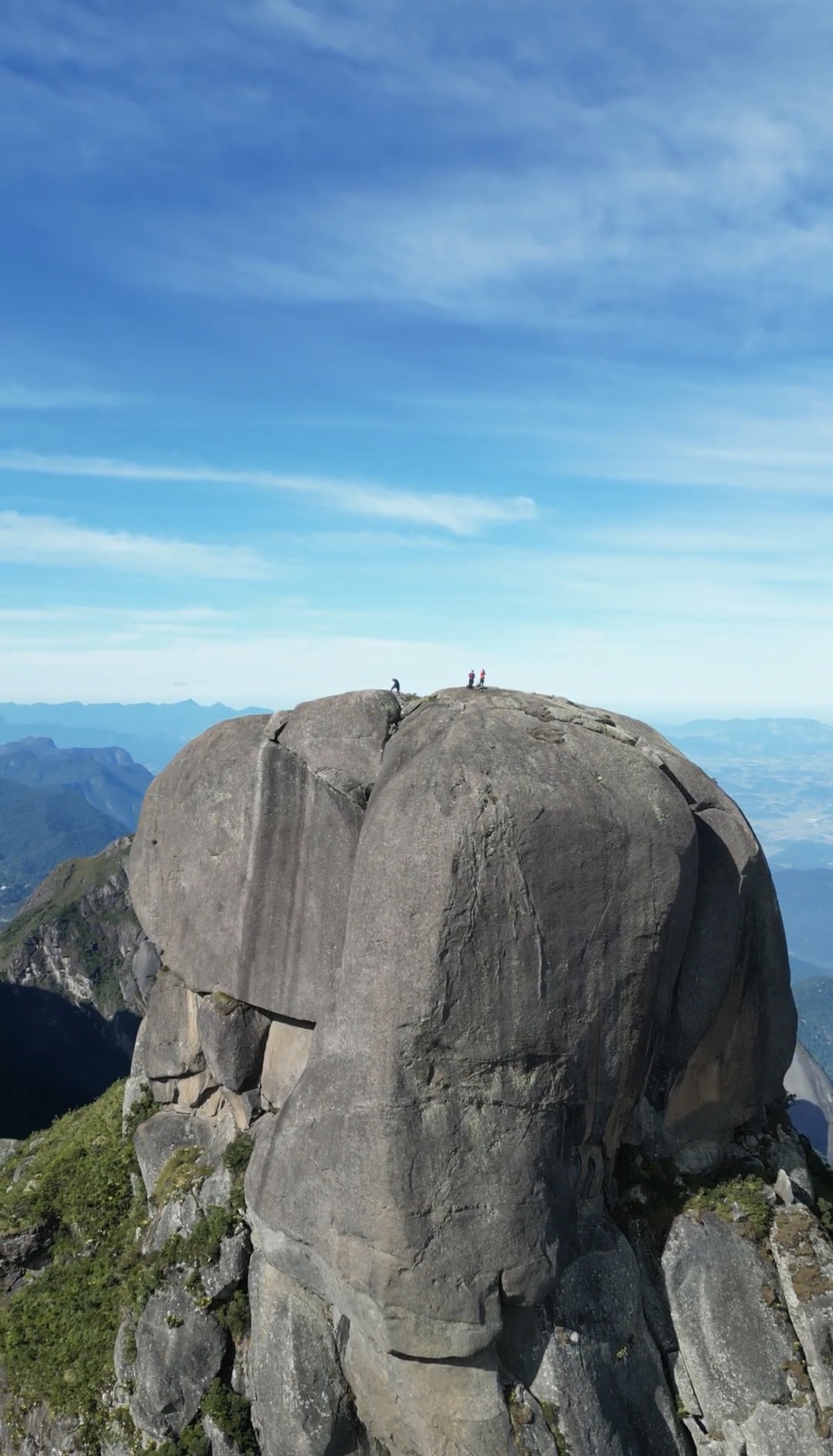Vista do cume arredondado do Garrafão com dois escaladores no topo mostrando a escala da formação e o vale abaixo