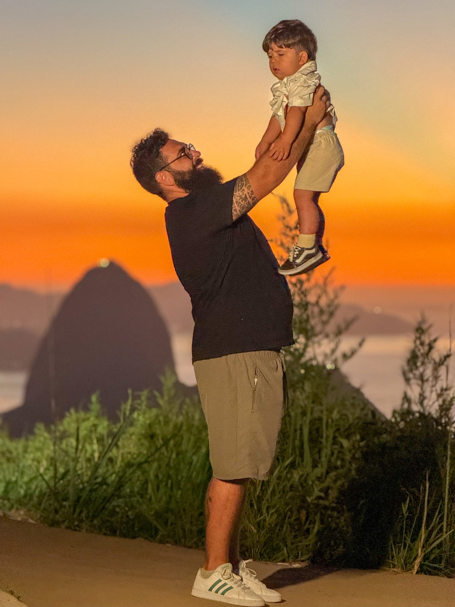 Pai levantando filho no Mirante Dona Marta com o Pão de Açúcar ao fundo no amanhecer laranja