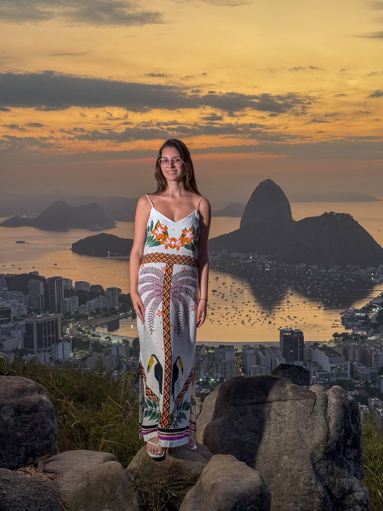 Visitante com vestido estampado no Mirante Dona Marta com o Pão de Açúcar e a Baía de Guanabara ao amanhecer dourado