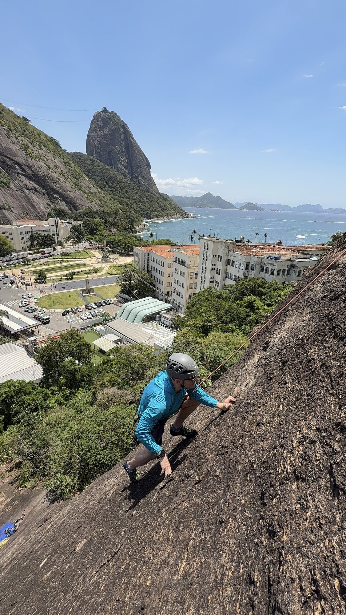 Escalador iniciante subindo a rocha do Morro da Babilônia com instrutor abaixo