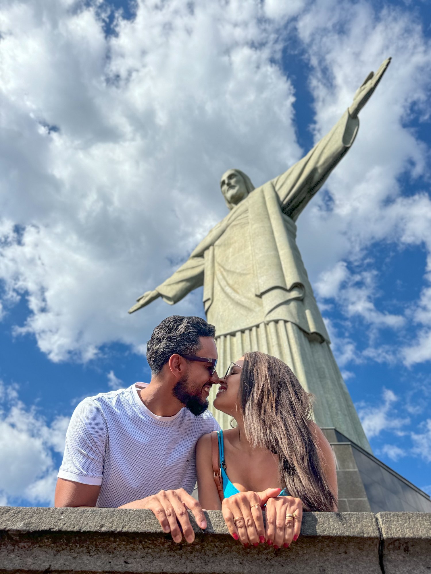 Casal embaixo do Cristo Redentor com braços abertos ao fundo