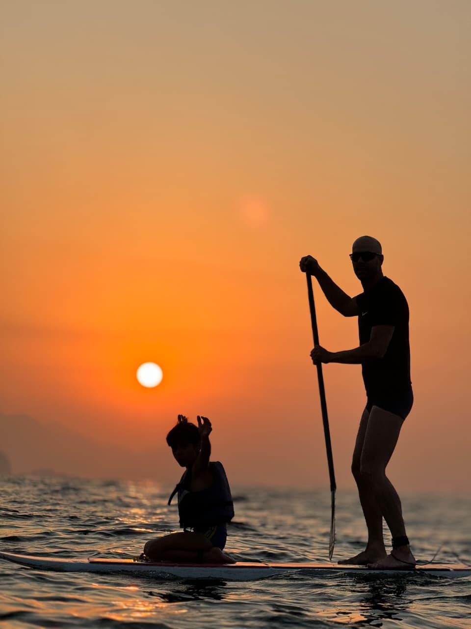Dupla praticando Stand Up Paddle em pé sobre as pranchas durante o nascer do sol em Copacabana