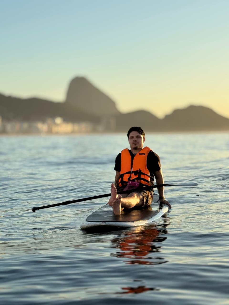Homem de colete salva-vidas no Stand Up Paddle com o Pão de Açúcar ao fundo na Praia de Copacabana