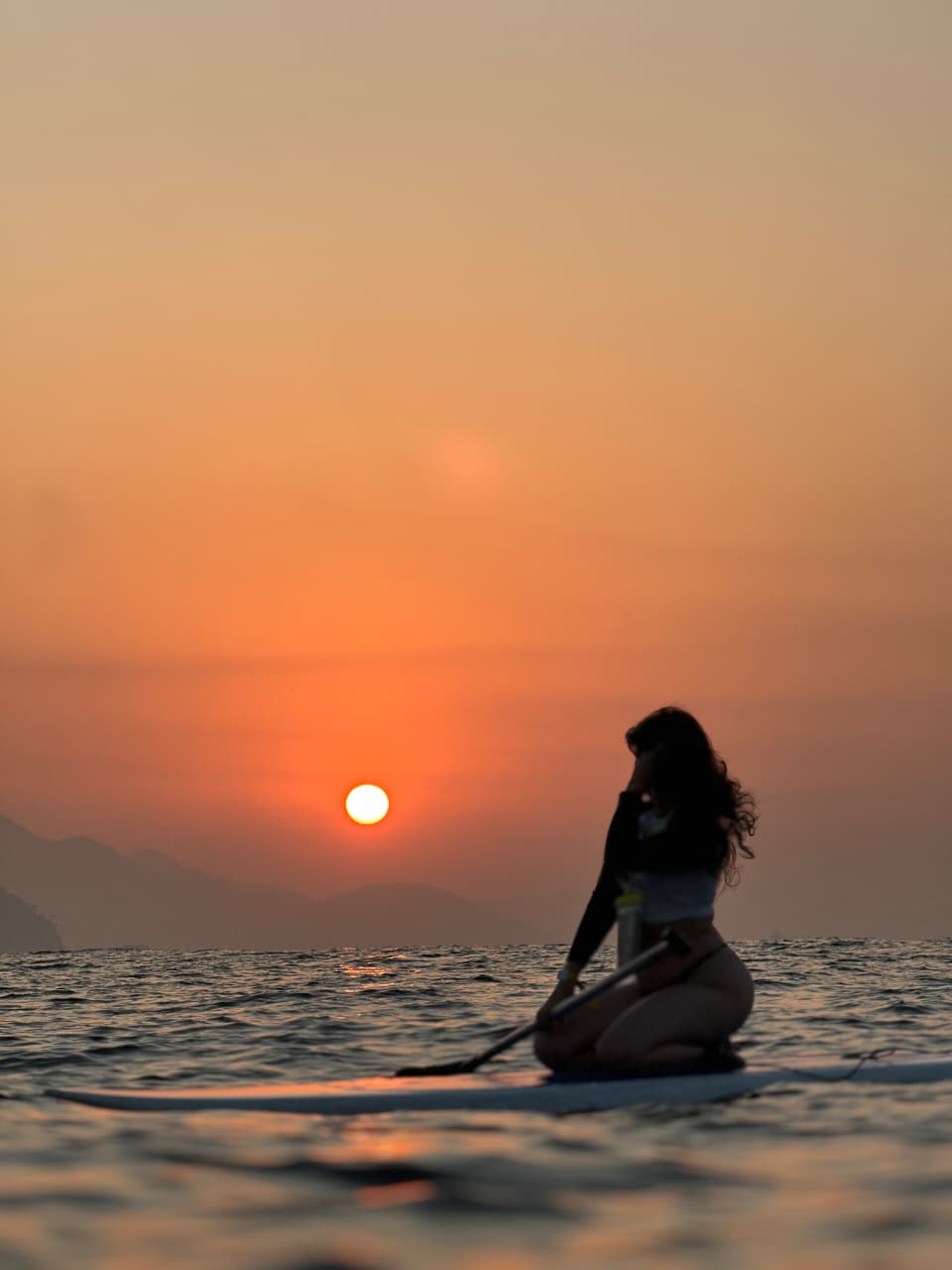 Praticante de Stand Up Paddle na prancha admirando o sol nascendo sobre o mar de Copacabana