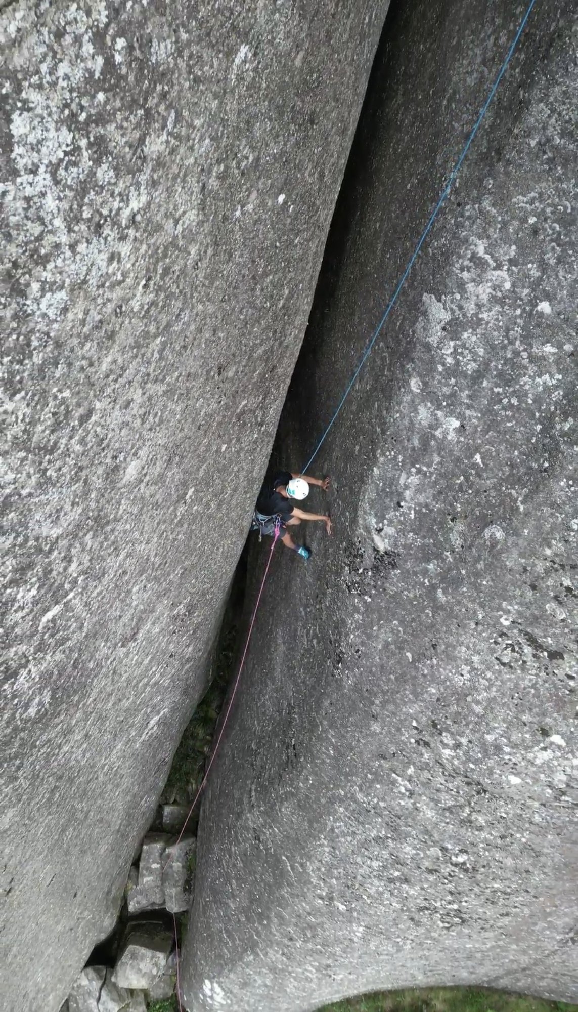 Escalador com capacete branco na passagem de chaminé entre dois grandes blocos de granito na Verruga do Frade