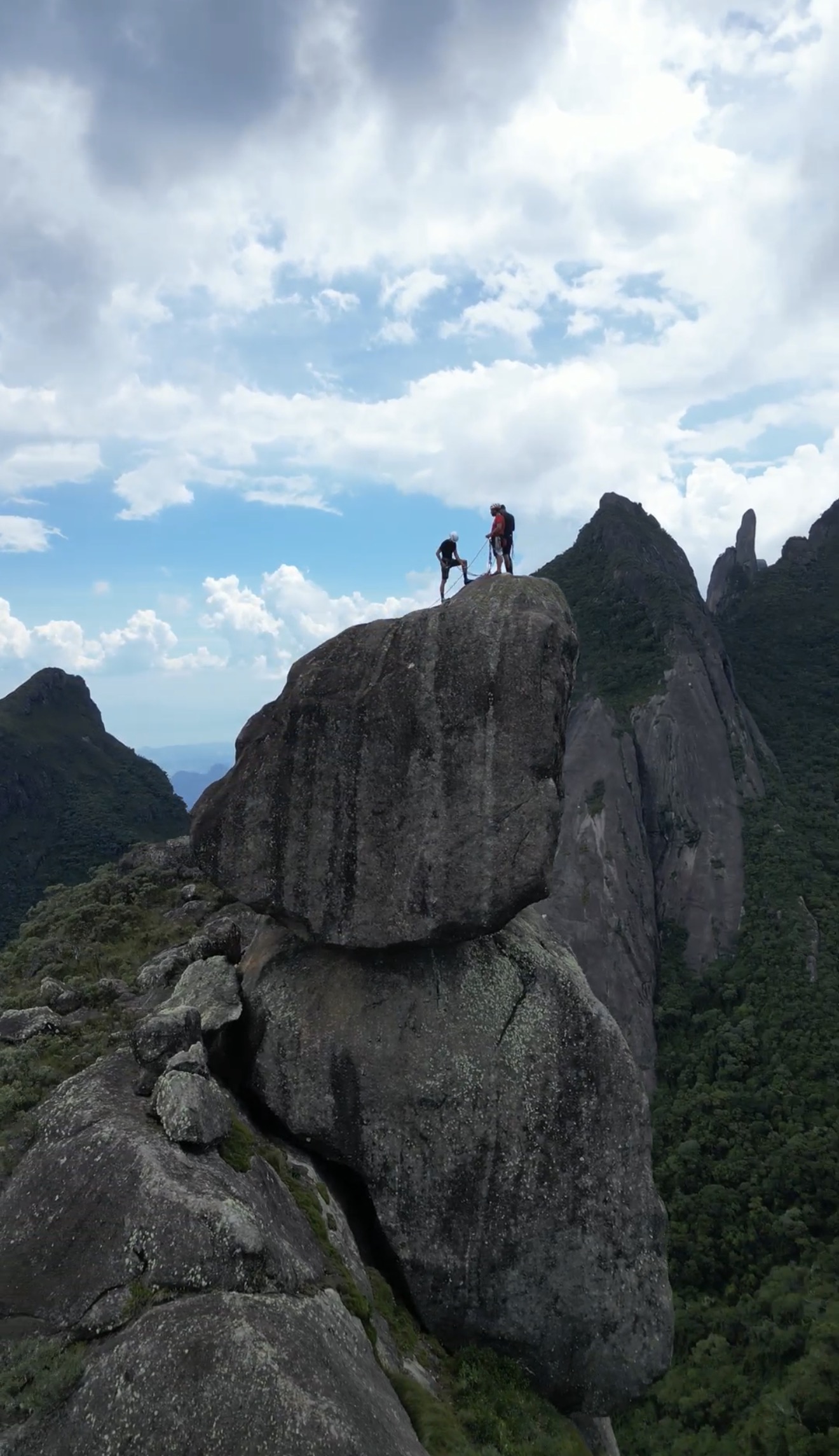 Dois escaladores no cume da Verruga do Frade com as torres da Serra dos Órgãos — Dedo de Deus e Dedo de Nossa Senhora — ao fundo